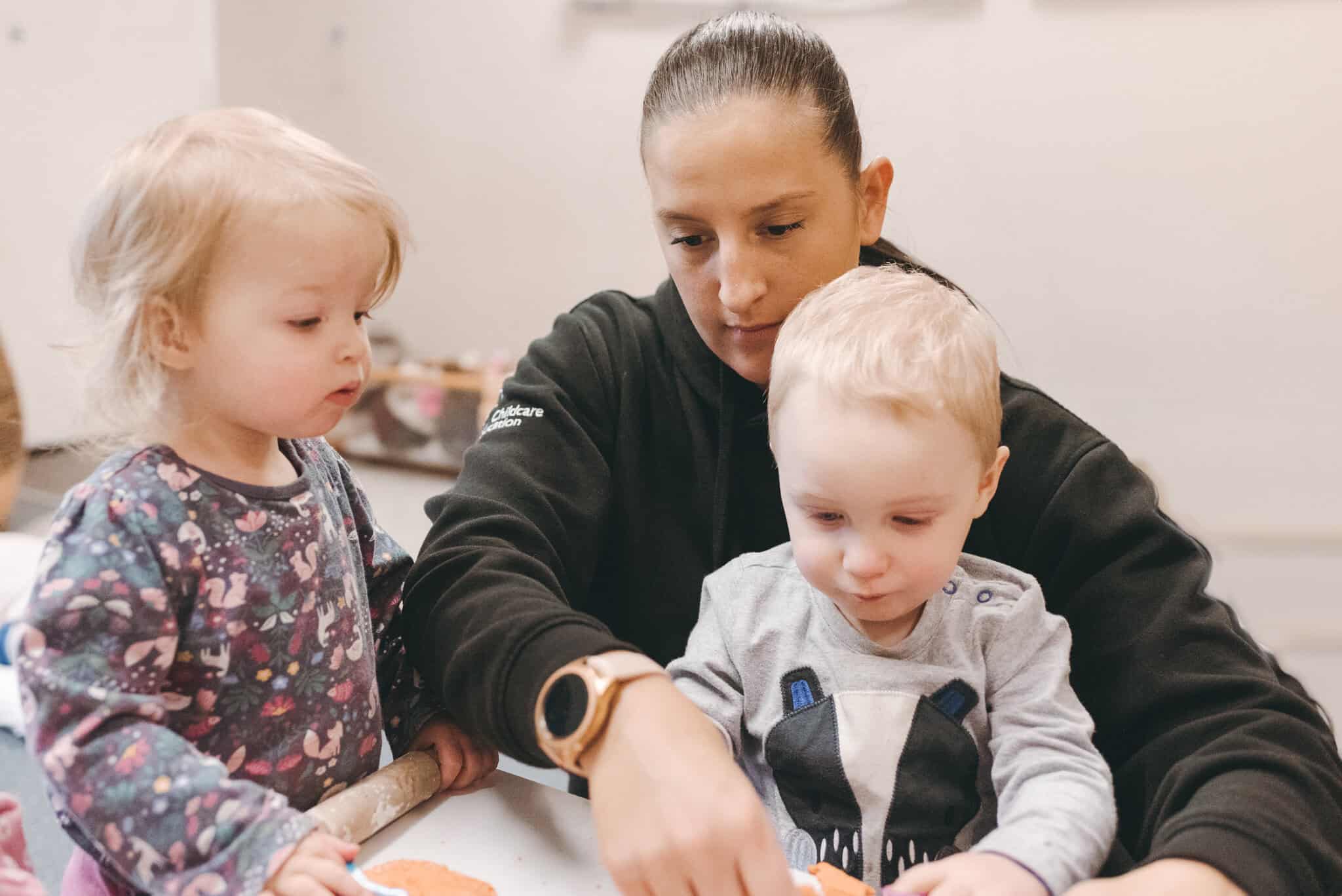 Caring childcare professional engaging with young children in a nurturing preschool environment, promoting early childhood development and learning at Thrive Childcare.