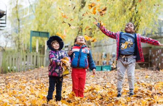 Bright children playing and enjoying autumn leaves at Thrive Childcare outdoor playground in a colourful, safe environment for early childhood development and exploration.