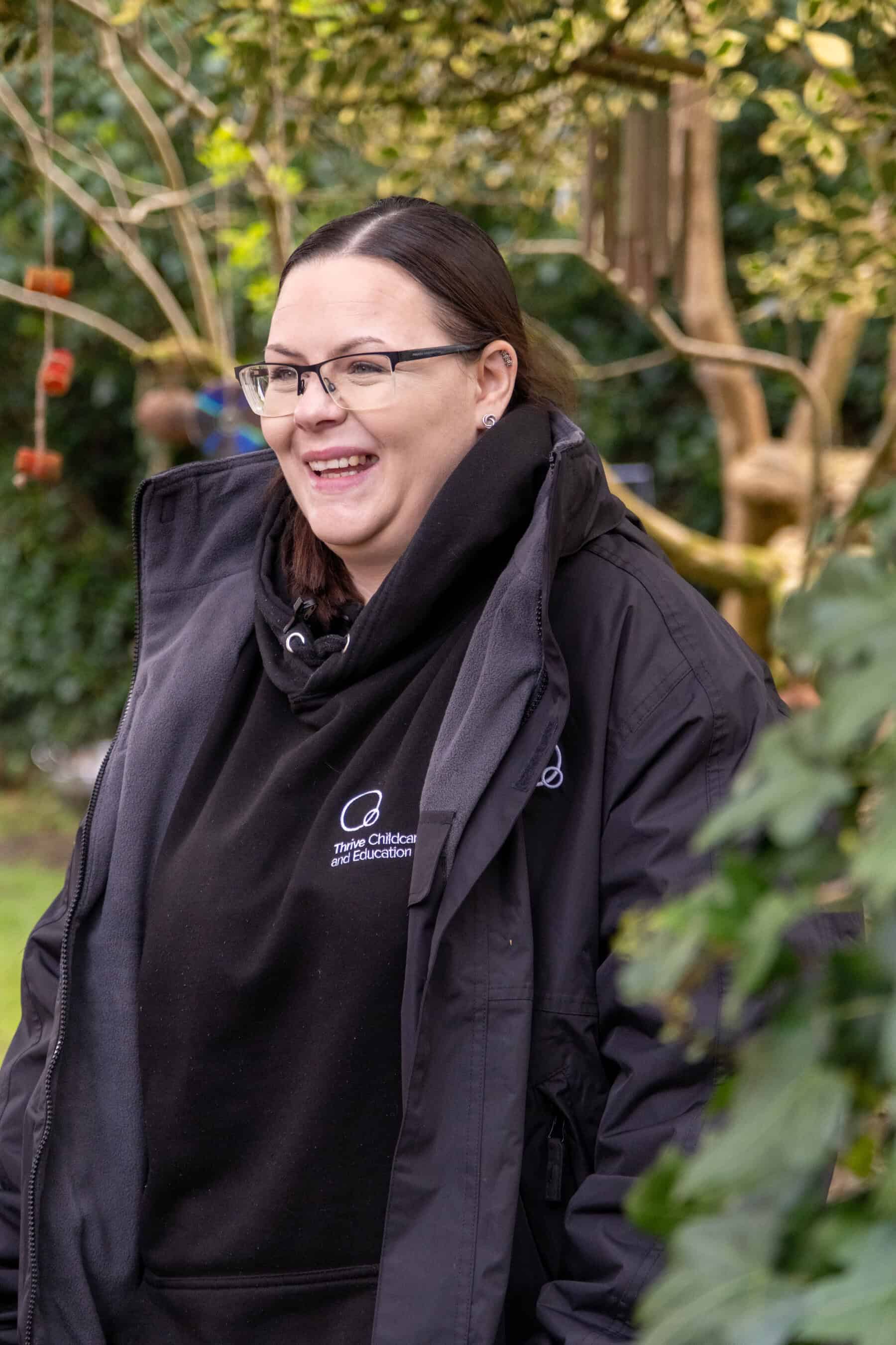 Friendly childcare professional outdoors at Thrive Childcare, engaging children with nature and play-based activities in a lush garden setting.