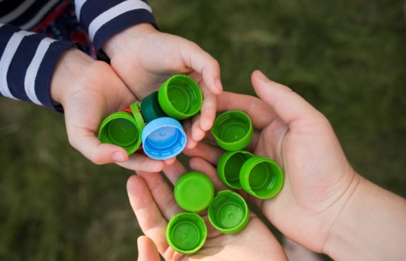 Child’s hands holding colourful plastic bottle caps, outdoor play, fostering fine motor skills, suitable for early childhood education and care at Thrive Childcare, promoting creative activities.