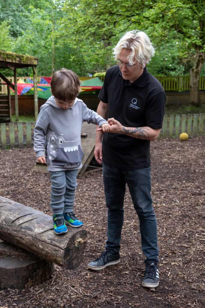 Supportive childcare professional assisting a young child outdoors at Thrive Childcare, fostering development and confidence in a natural play environment.