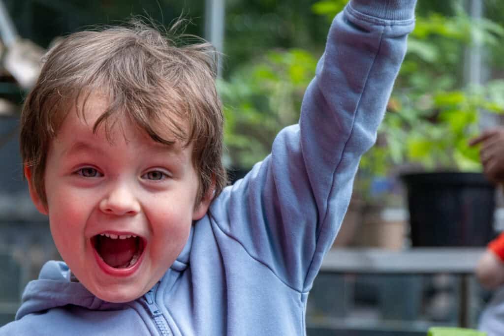Energetic young boy joyfully raising hand, playing outdoors at Thrive Childcare, fostering growth and development in a nurturing environment for children.