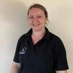 Bright-eyed childcare professional smiling in Thrive Childcare uniform in a welcoming nursery environment.
