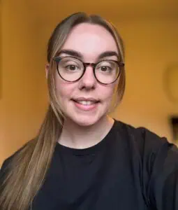 Friendly woman with glasses smiling at camera in a bright childcare setting, promoting certified early childhood education and safe, nurturing environment at Thrive Childcare.