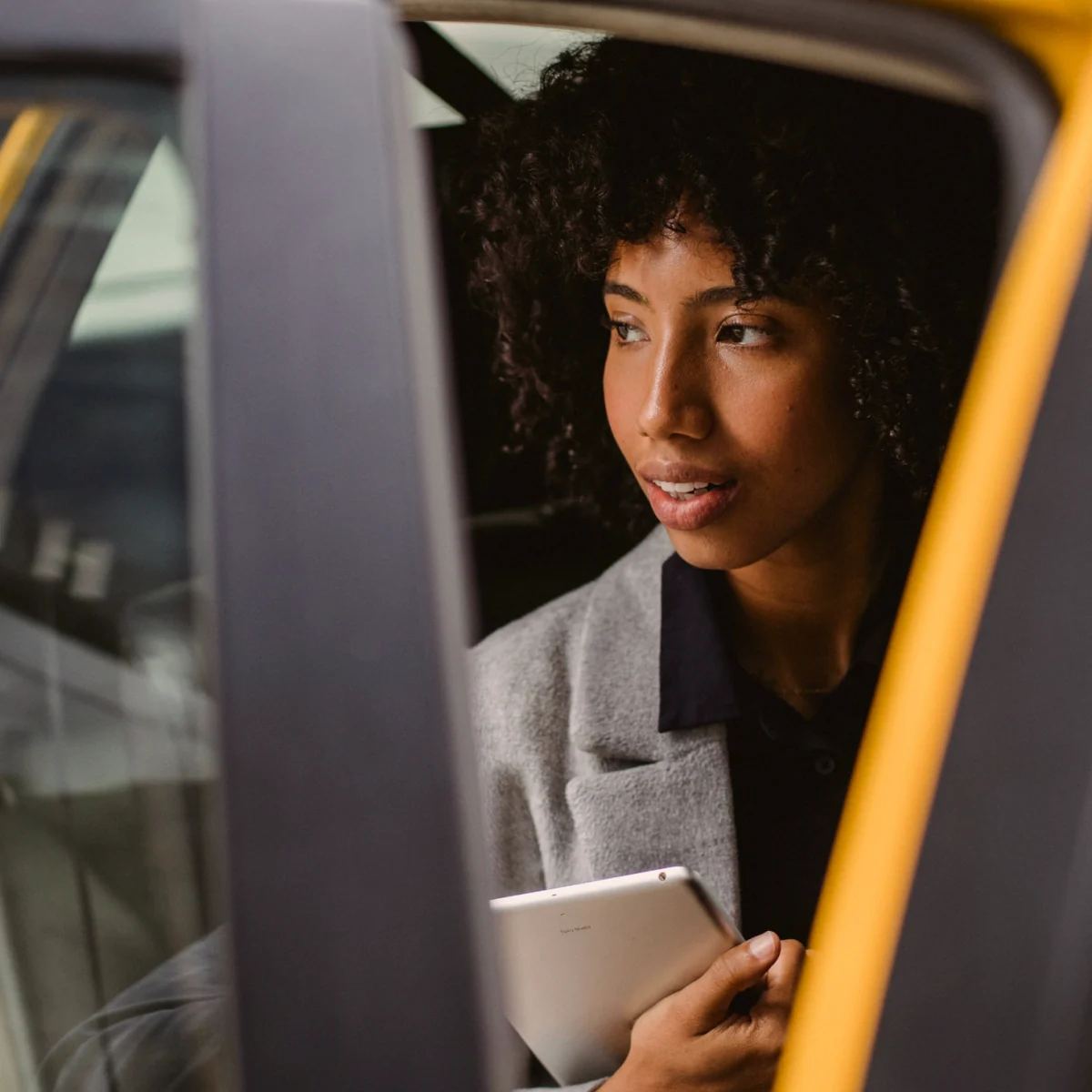 A woman looking out of a taxi door while holding a tablet