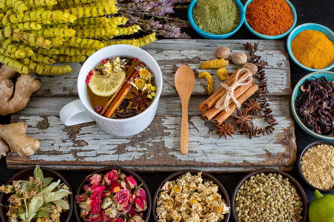 Cup of herbal tea with lemon, cinnamon and star anise surrounded by dried flowers, herbs and spices – Yukiko Nutrition