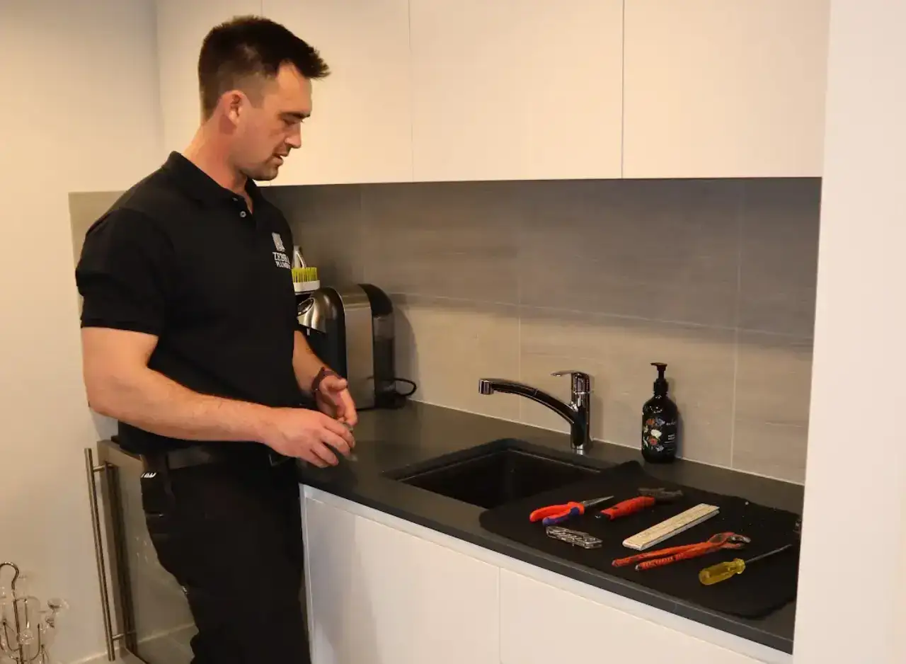 Plumber preparing tools to carry out hot water plumbing repairs in a modern kitchen.