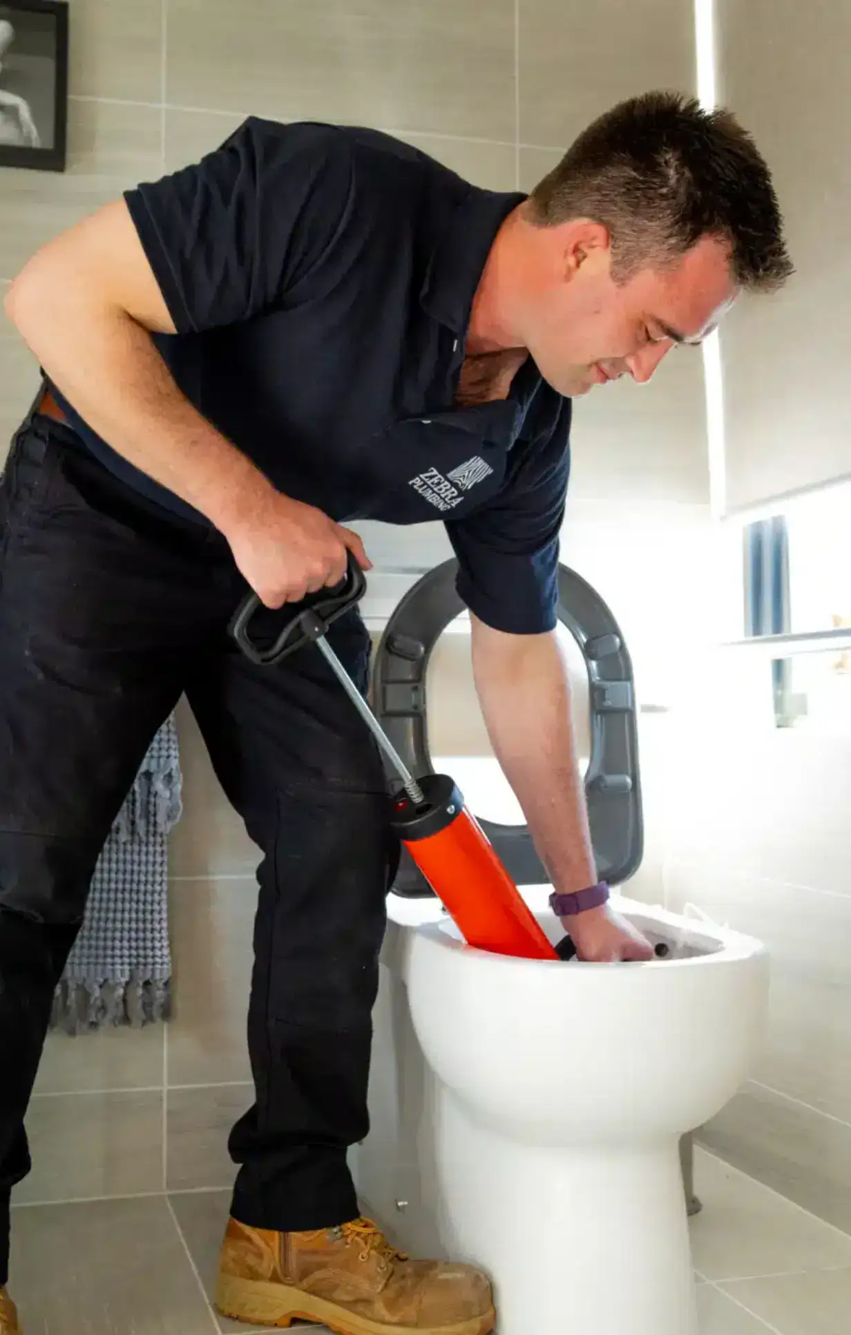 Professional plumber unclogging a toilet with a specialised drain tool during a toilet repair service.