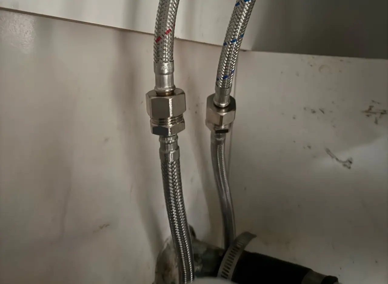 Plumbing pipe fittings with flexible hoses and metal connectors in a bathroom setting.