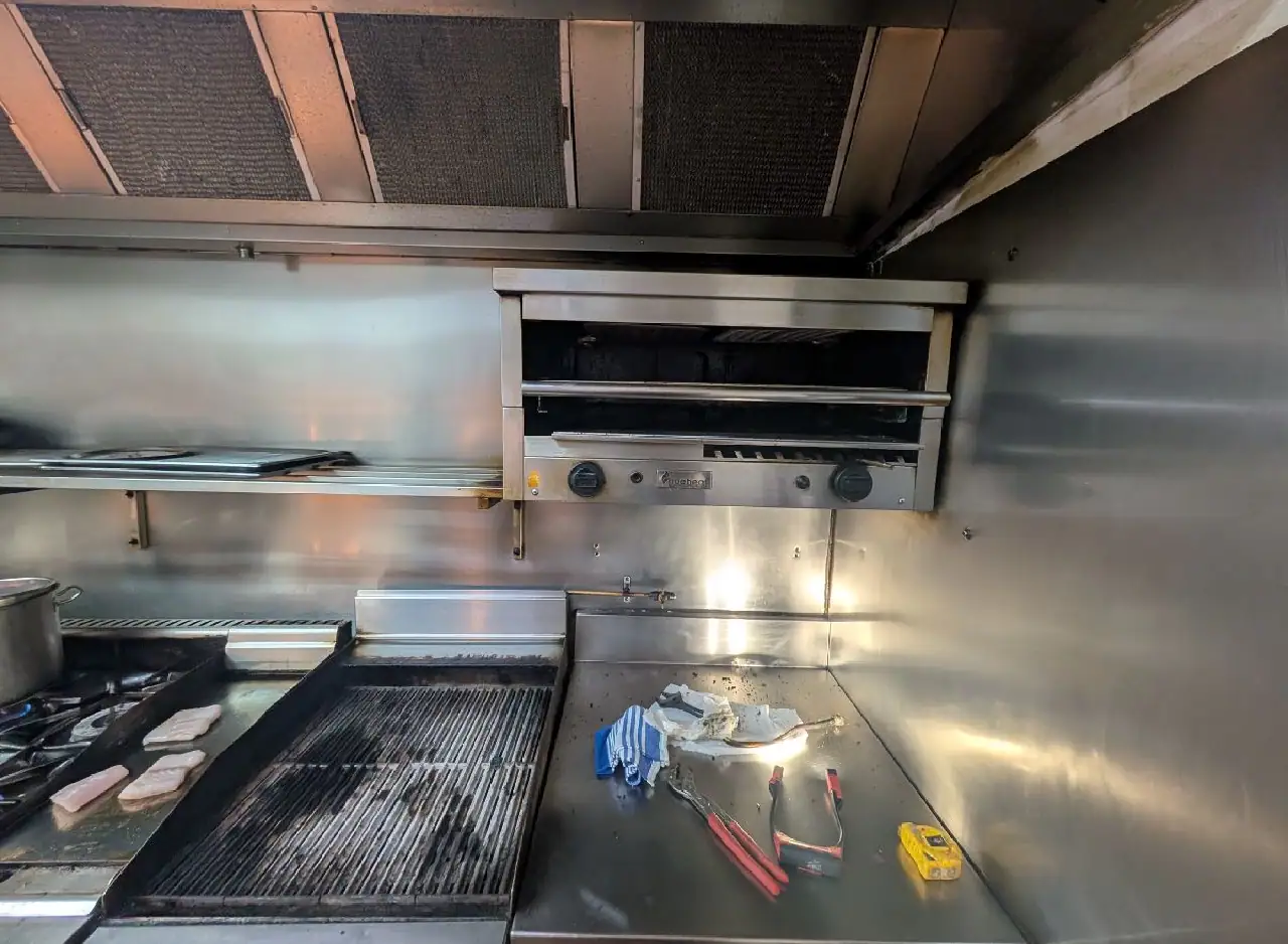 Industrial kitchen stainless steel cooking area with grill and oven equipment.