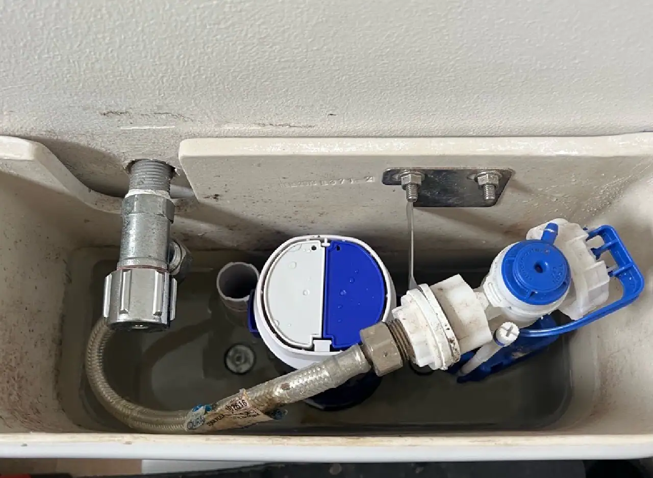 Close-up of toilet tank with plumbing components and water level control.