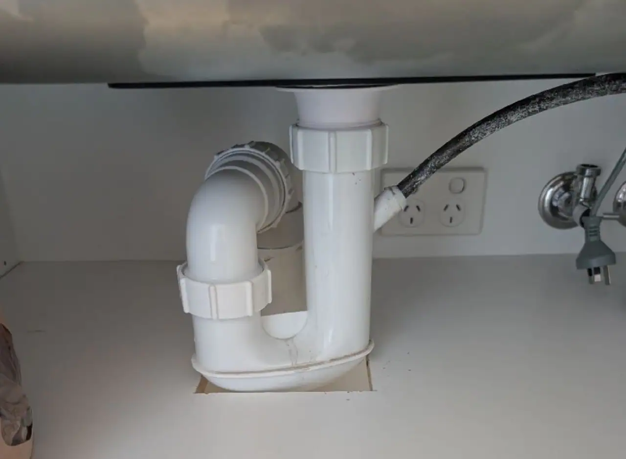 PVC pipe plumbing under sink for drainage and water supply.