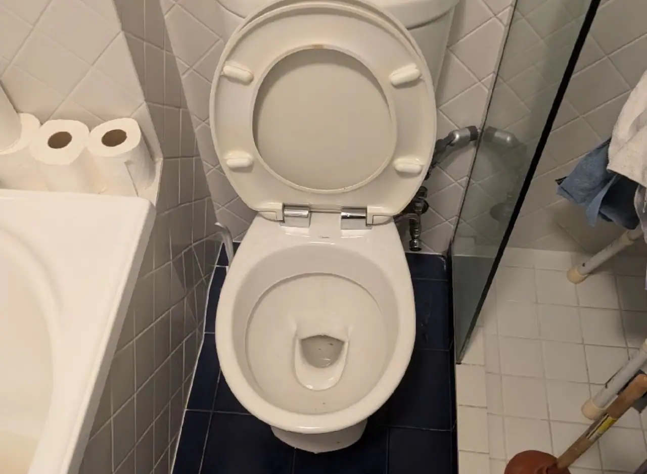 Toilet with open lid in a bathroom, showcasing plumbing and hygiene fixtures.