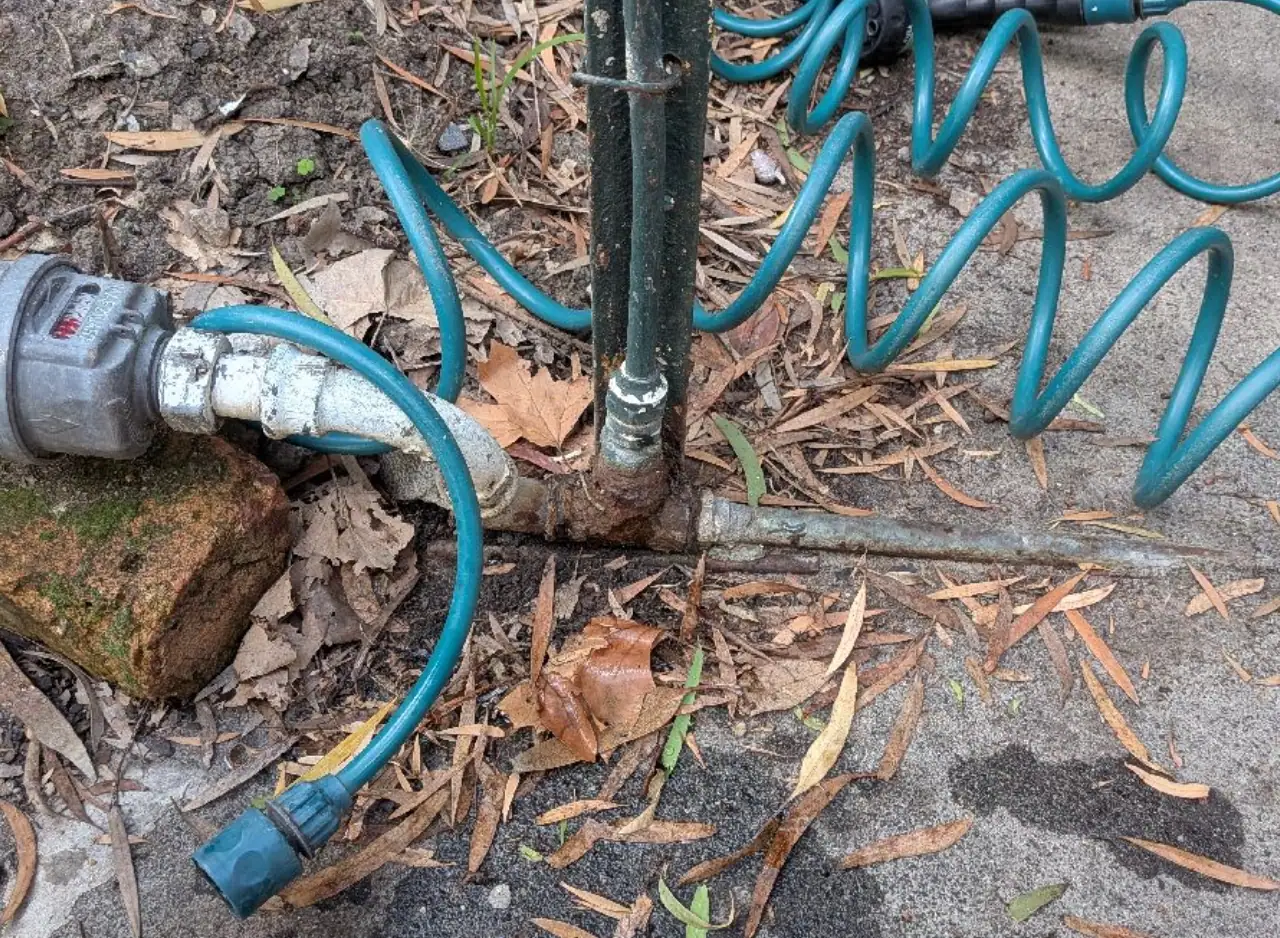 Outdoor plumbing pipe connection with hoses and fittings in garden or yard.