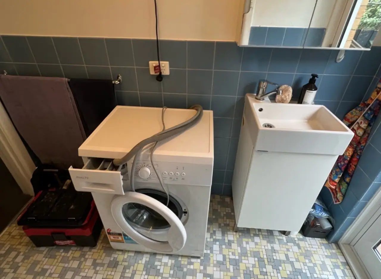 Washing machine with laundry basket and sink in a small laundry room.