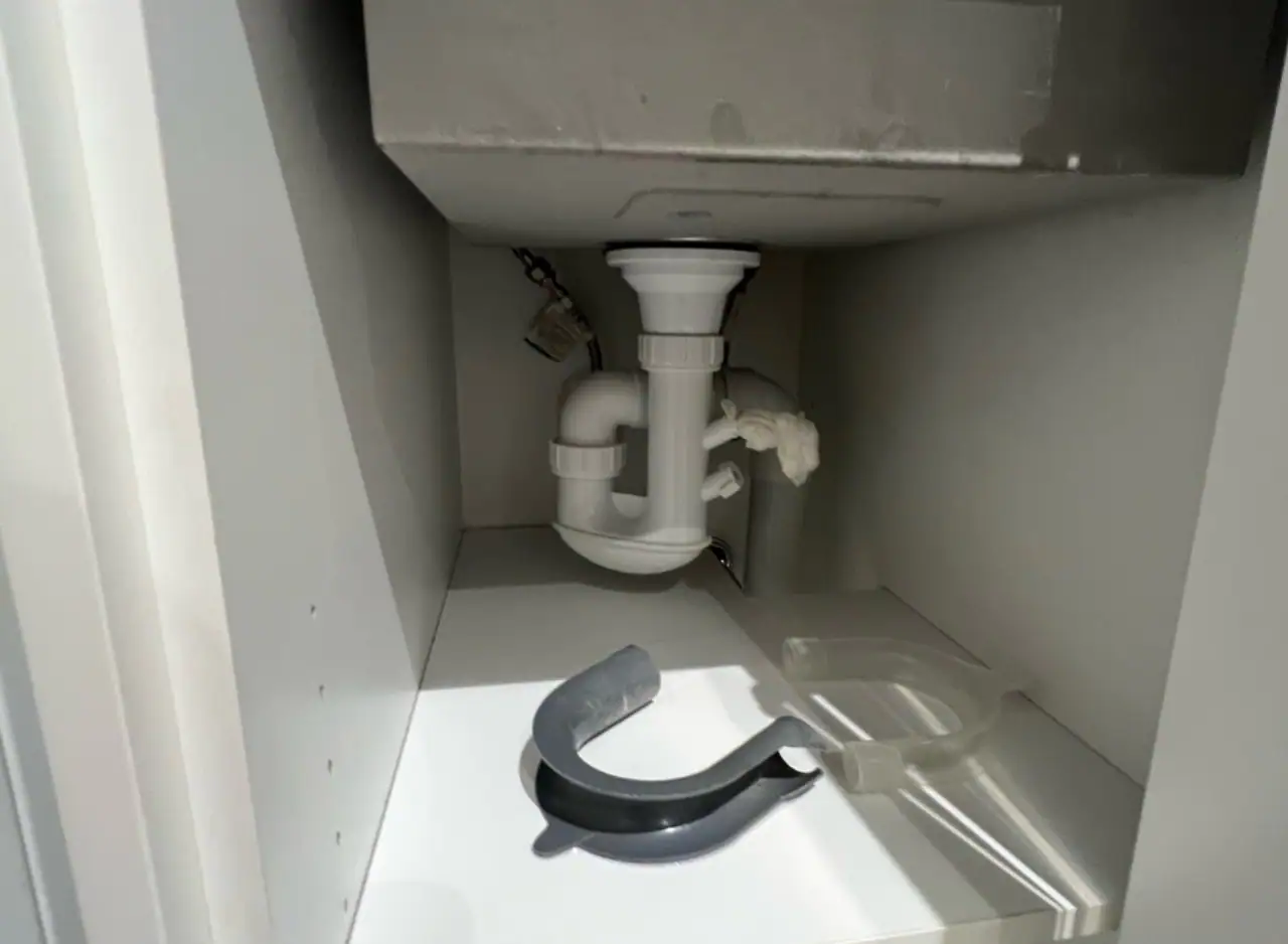 Drain pipe under kitchen sink with plumbing components.