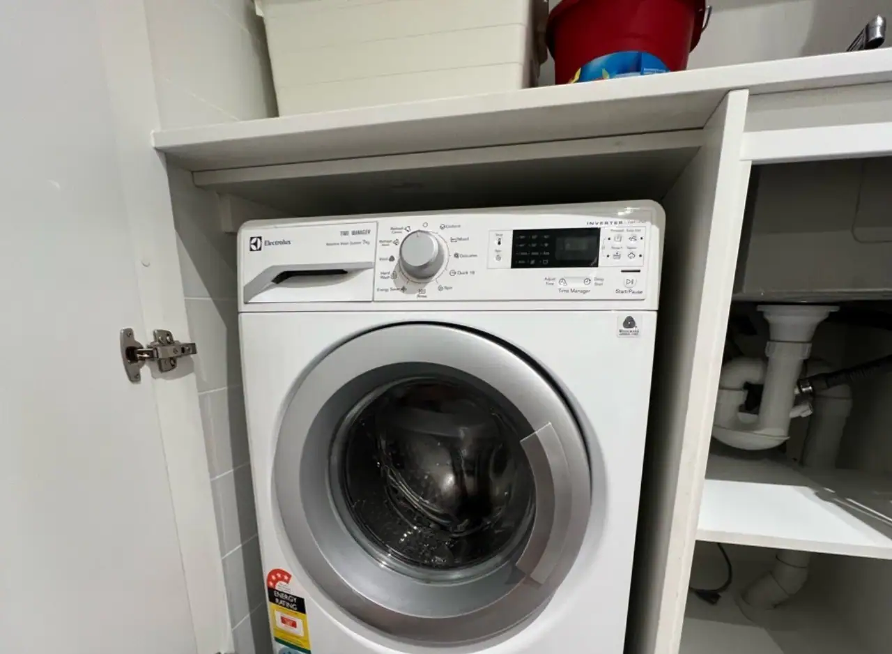 Front-loading washing machine installed in laundry room with plumbing connections.
