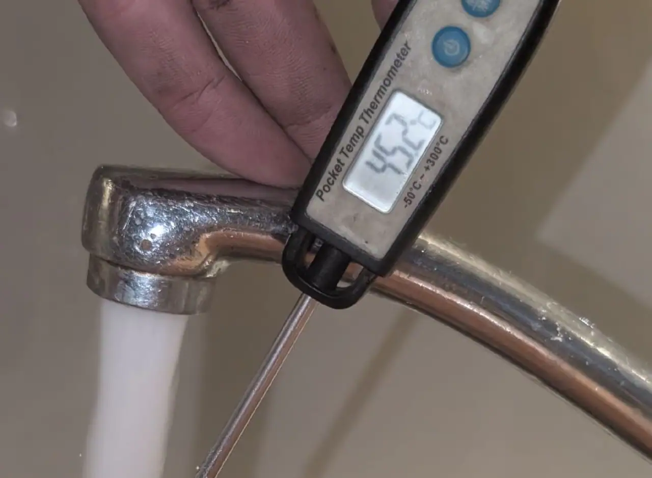 Thermometer measuring water temperature at 45.4°C on a hot water tap.