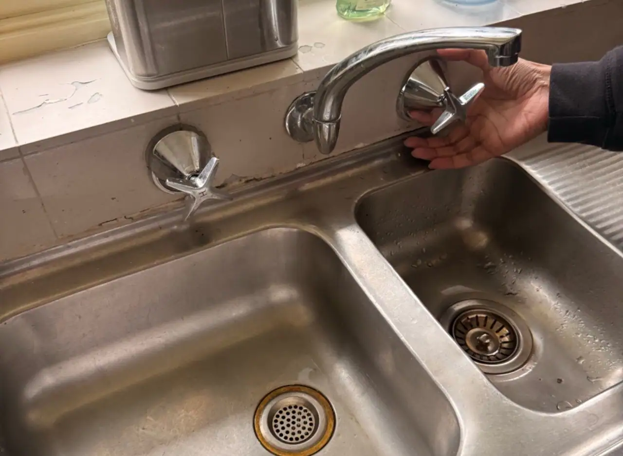 Hand fixing kitchen sink faucet to resolve water hammer issue.