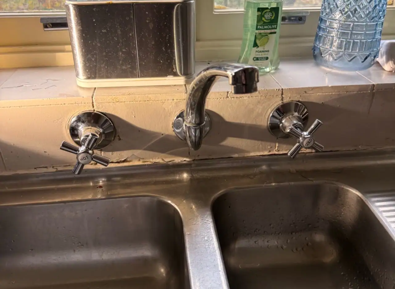 Kitchen sink with a leaking faucet and cleaning supplies nearby.