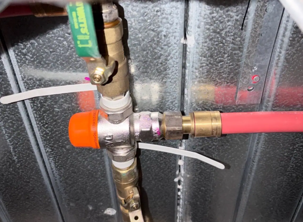 Brass plumbing pipes and fittings with white and pink tubing connections, orange shut-off valve, and green level tool