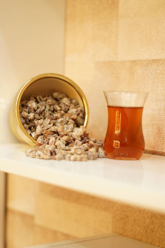 Flavored chopped dates in a gold pot beside a glass of tea