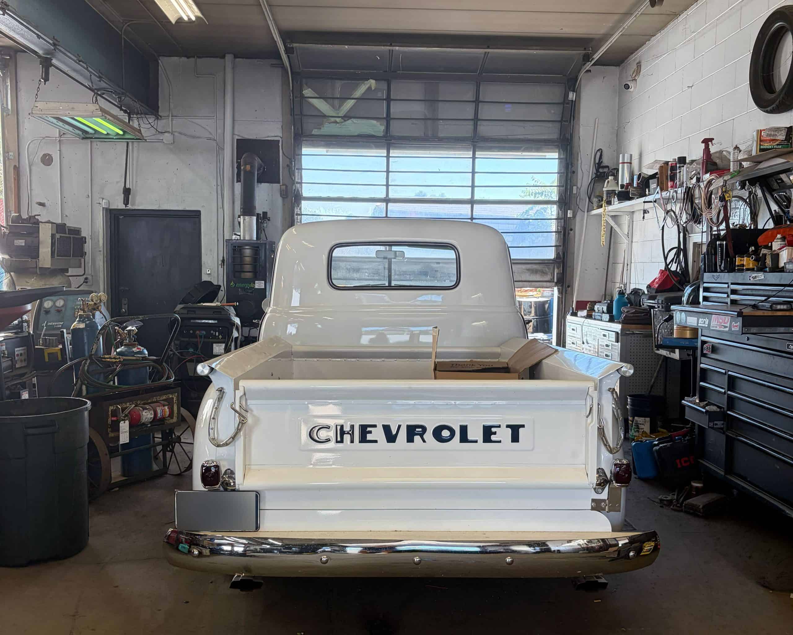 Restored Chevrolet pickup truck inside auto repair shop with tools and equipment.