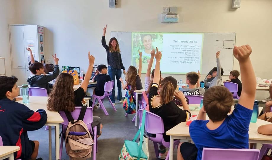 a woman giving lecture to kids in school raising their hands in participation