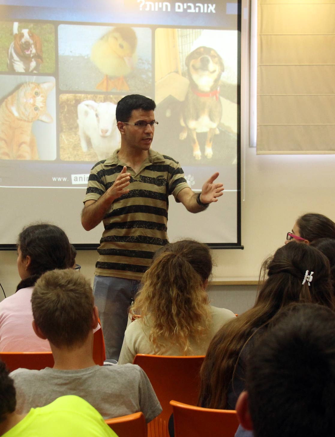 man giving lecture to kids with a slideshow about animals behind him