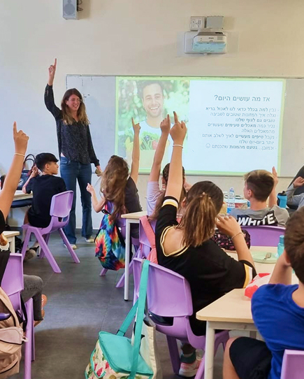 a woman giving lecture to kids in school raising their hands in participation