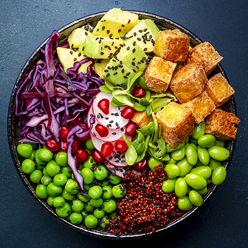 Vegan buddha bowl with red quinoa, fried tofu, avocado, edamame beans, green peas, radish, cabbage, pomegranate  and sesame seeds with soy sauce. Healthy diet food. Blue table background, top view