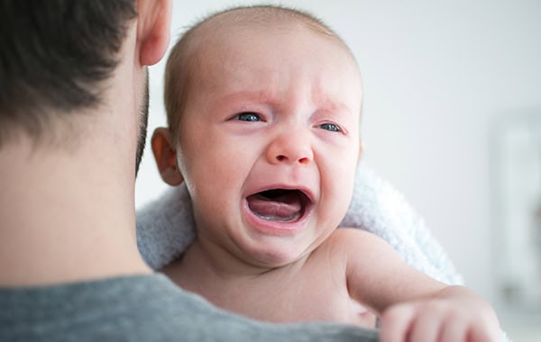 Over shoulder view of man carrying crying baby son