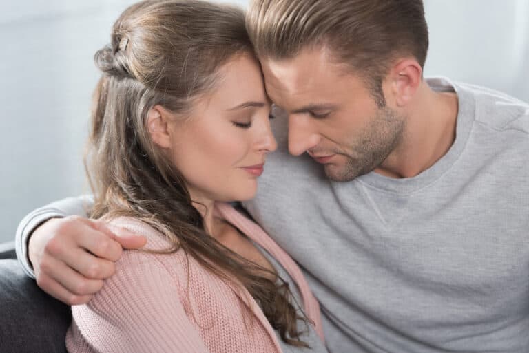 A couple comforting each other on the couch as they hug.