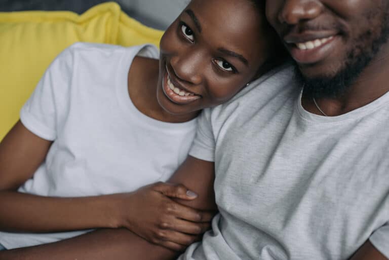 A young couple smiling on the couch as they hug.