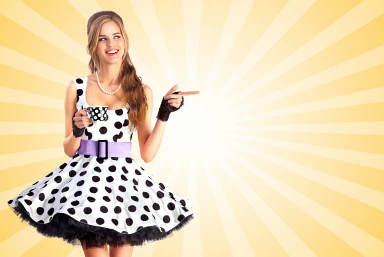 Creative vintage photo of a beautiful pin-up girl in a polka dot dress, holding a cup of tea and pointing aside on colorful abstract cartoon style background.