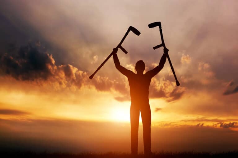 Man raising his crutches at sunset.