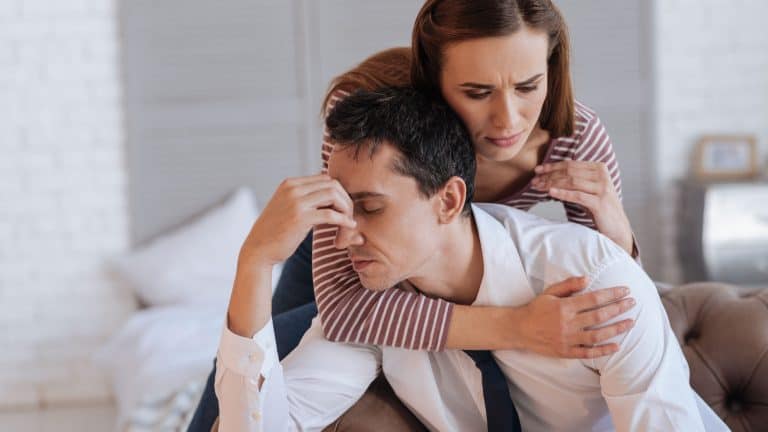 Warm hugs. Cheerful kind loving woman looking friendly and supporting while hugging her depressed exhausted husband