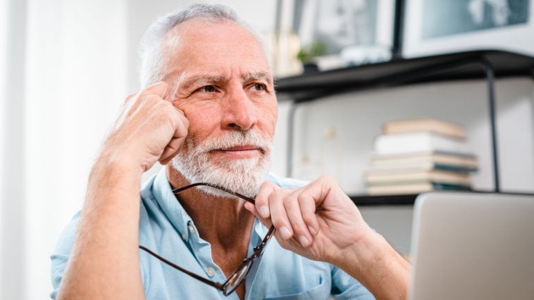 Tired mature 60s man working at laptop from home, taking off glasses, touching head and eyes. Old male pensioner suffering from headache, dizziness after looking at computer screen. Eye sight problem