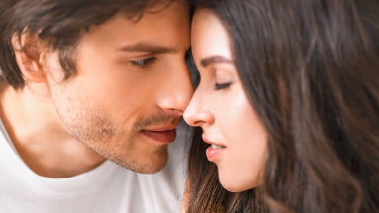 This is a close-up portrait of a man and a woman about to kiss. They are looking into each others eyes and appear to be in love.