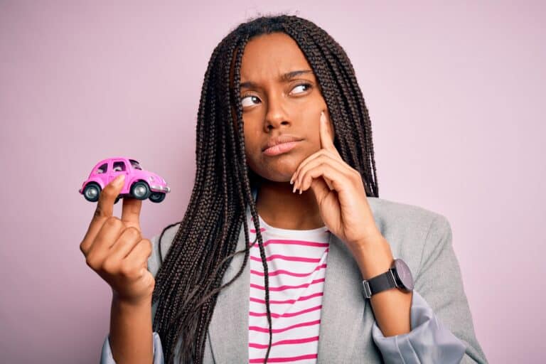 Young african american girl holding small car as transport insurance over isolated pink background serious face thinking about question, very confused idea