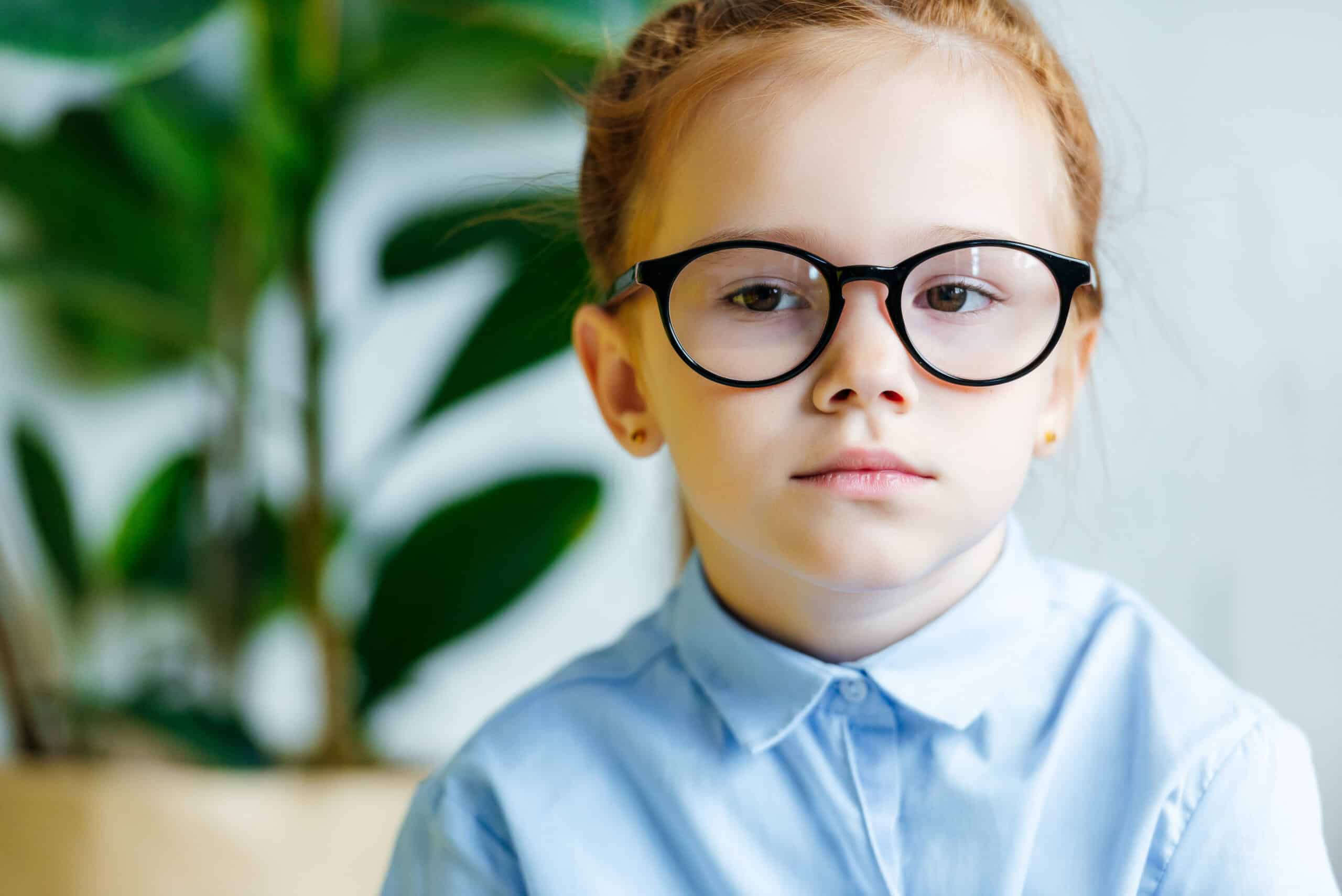 beautiful little redhead child in eyeglasses looking at camera