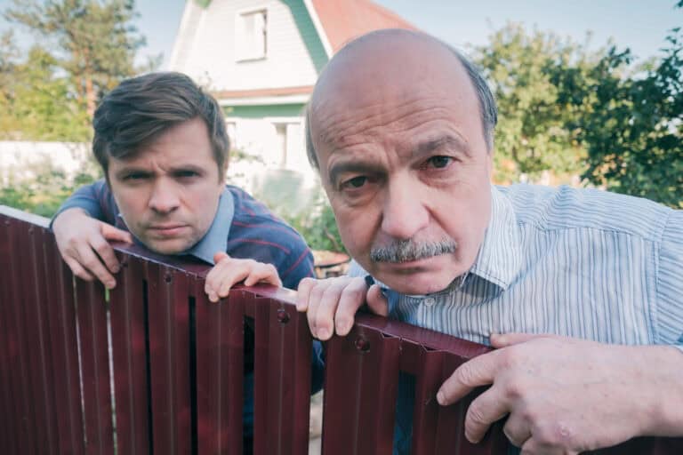 Two caucasian men carefully watching over the fence.