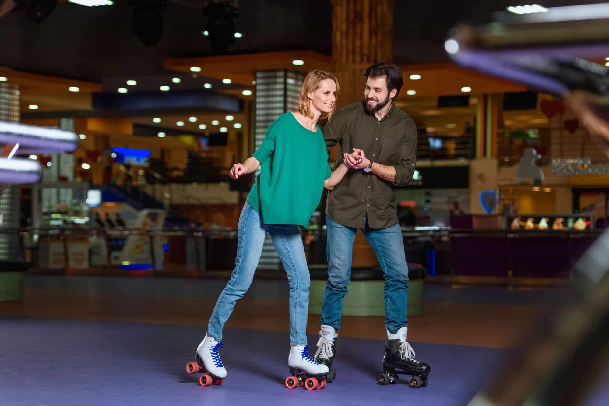 Young couple holding hands while skating together on roller rink
