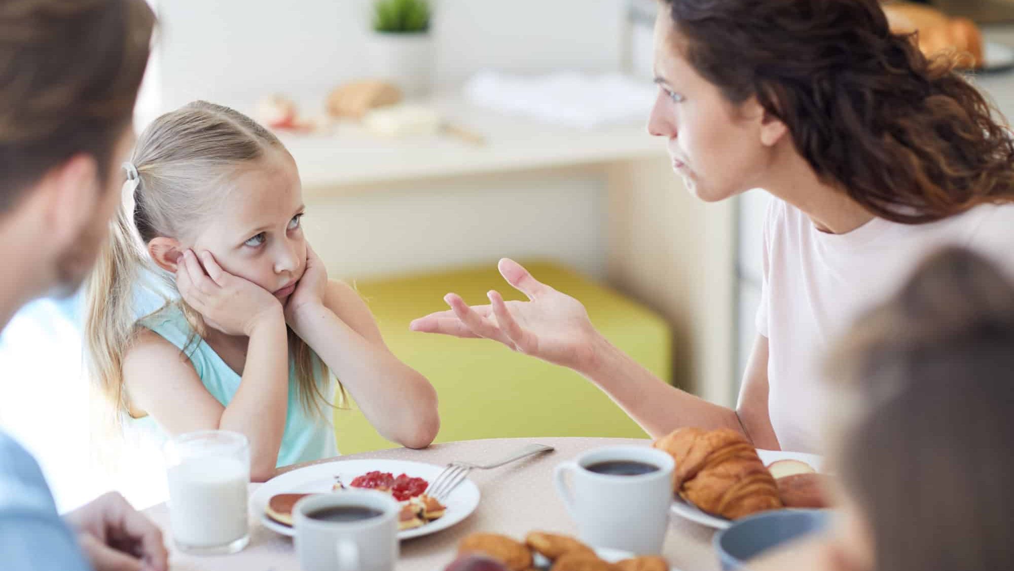 Strict mother scolding one of little daughters by breakfast because of bad behavior