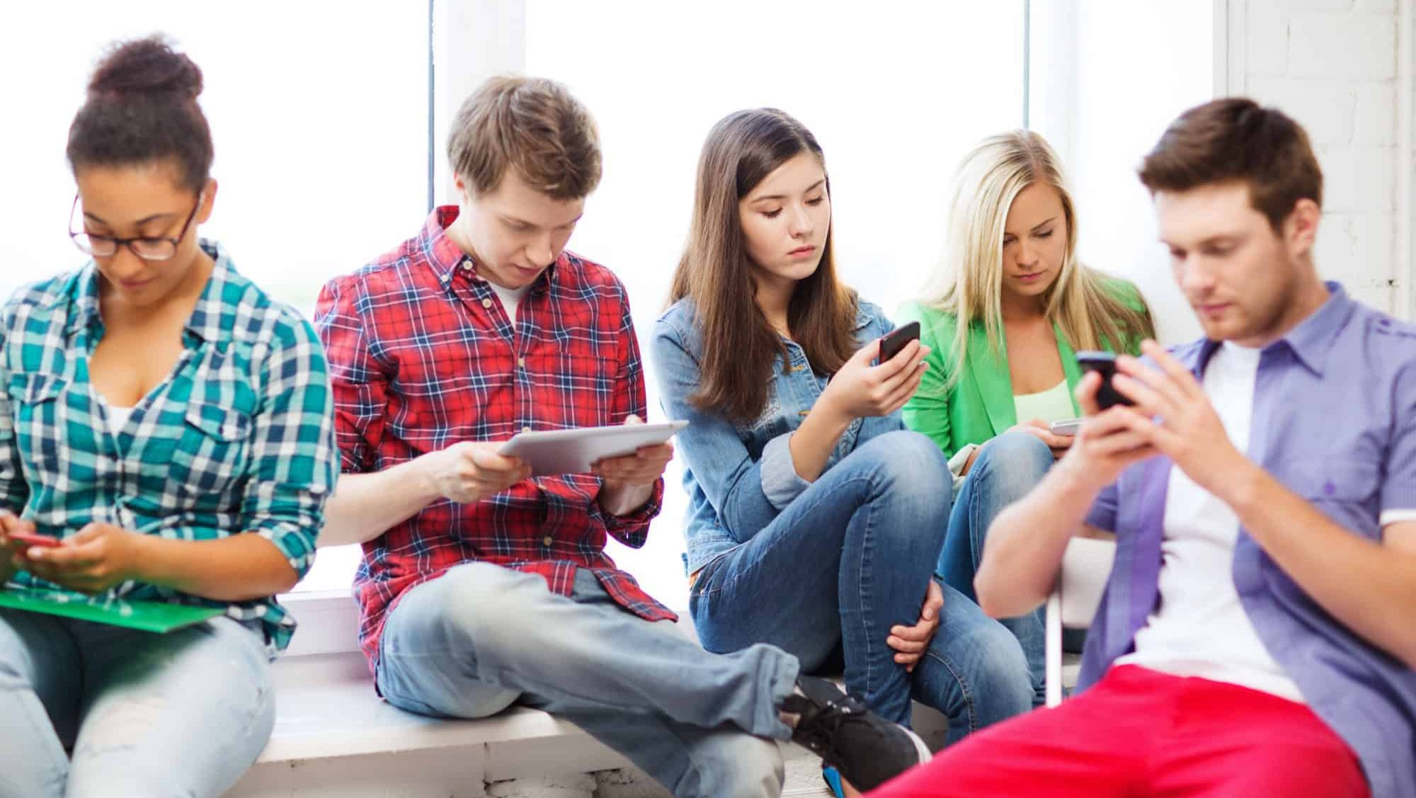 education and internet concept - students looking at their phones and tablet pc at school