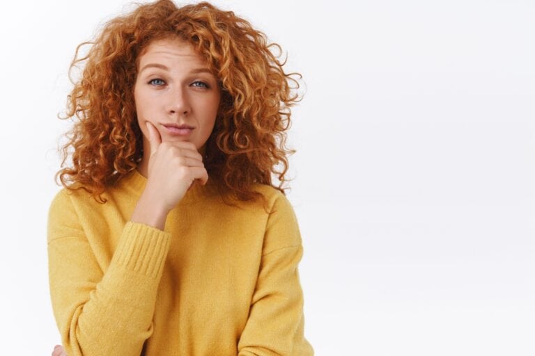 Skeptical, judgemental redhead woman with curly hair, rub chin and squinting as looking camera, give-out her opinion, thinking or sharing her impression, standing pensive white background