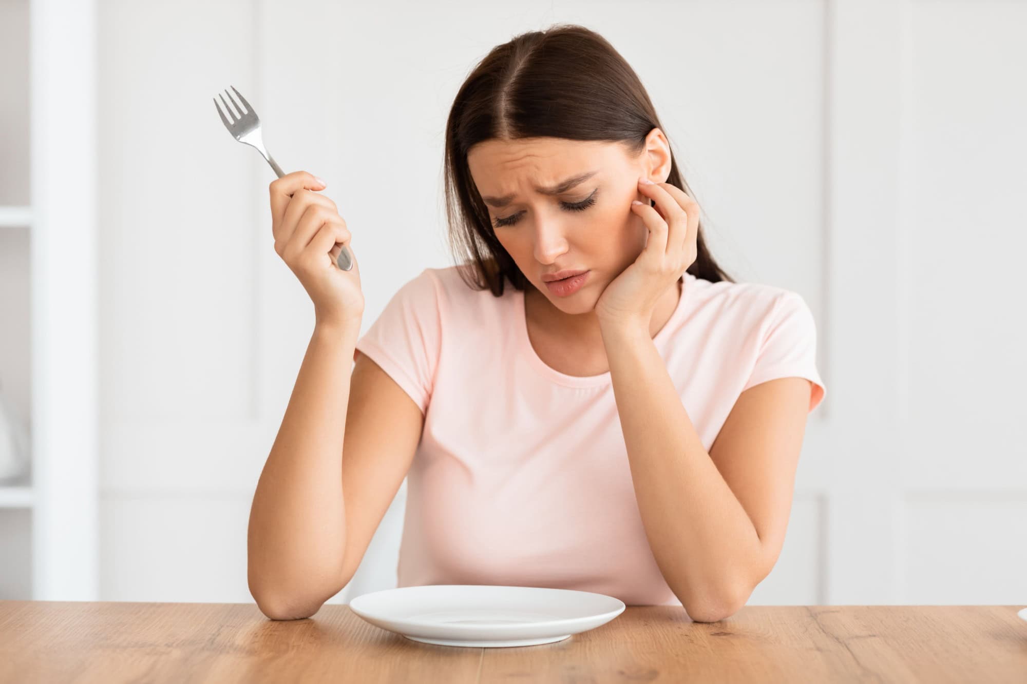 Unhealthy Dieting. Hungry Woman Looking At Empty Plate On Dinner Table Slimming On A Diet At Home.