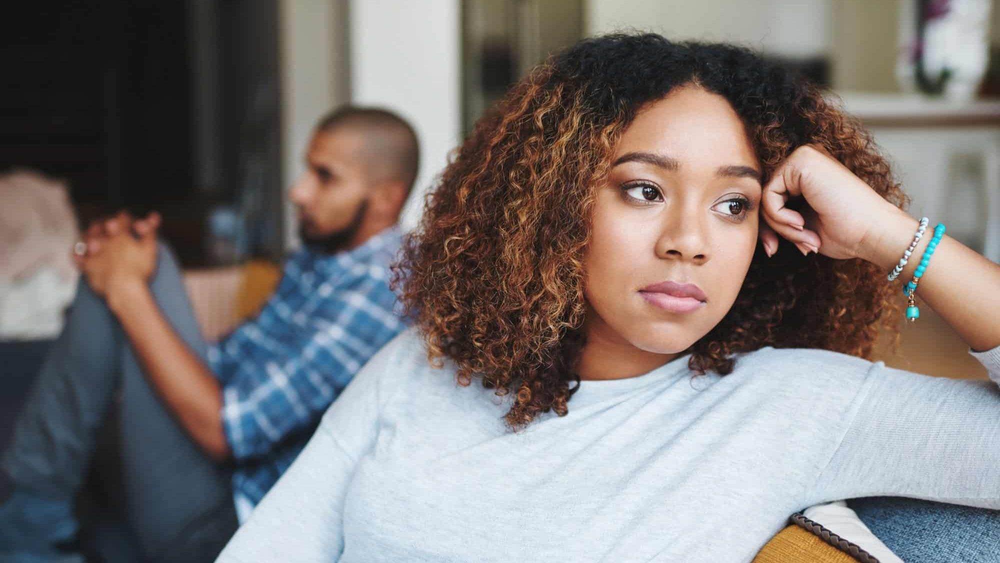 Unhappy couple and sad woman upset after argument or conflict with her man on home sofa. Angry girlfriend or female thinking about disagreement or ignoring partner, tired of relationship problems.