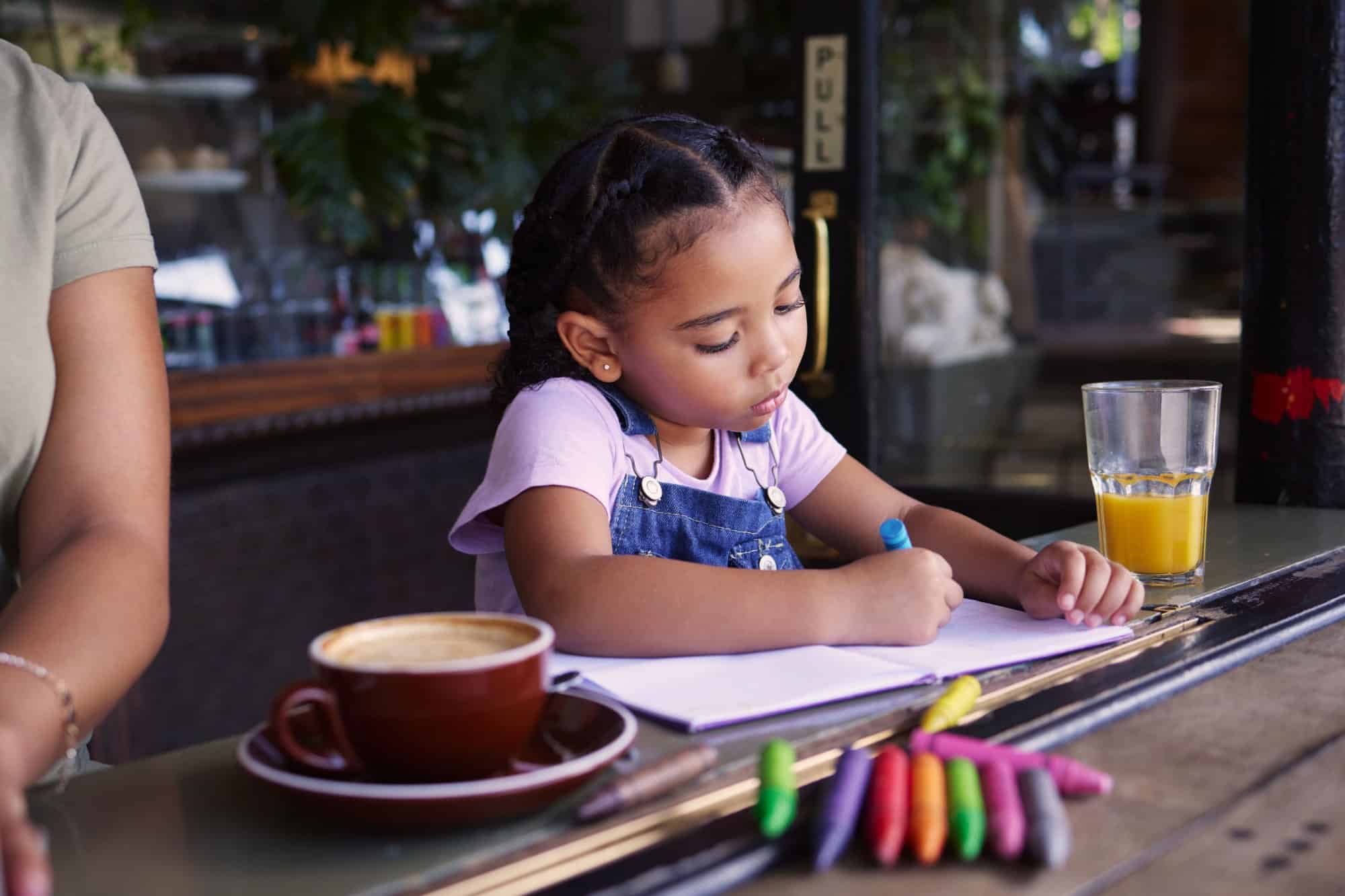 Girl child color in book at cafe, creative and drawing with crayons, family day to relax with learning and art in Atlanta. Young kid, growth and writing, education and creativity while at coffee shop