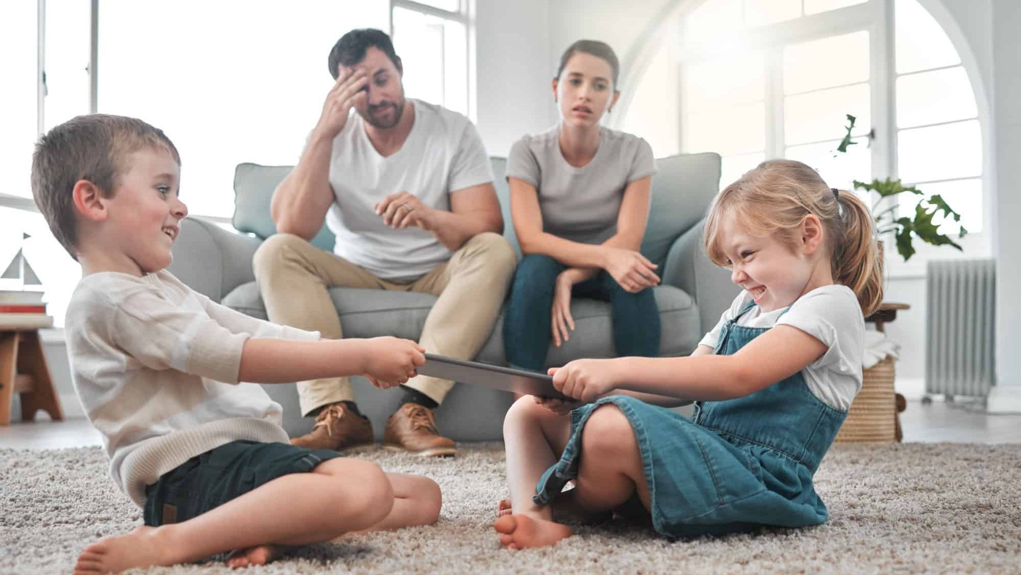Fight, argue and children with tablet in home with upset, frustrated and annoyed parents. Family, conflict and kids with digital tech to share for online games, cartoons and internet in living room